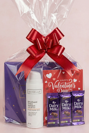 Valentine's Day gift set with skincare product, chocolate bars, and a red bow on a light pink background.